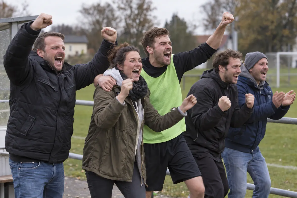 Symbolbild: Zuschauer und Ersatzspieler jubeln am Rand eines Amateur-Fußballplatzes über ein Tor.